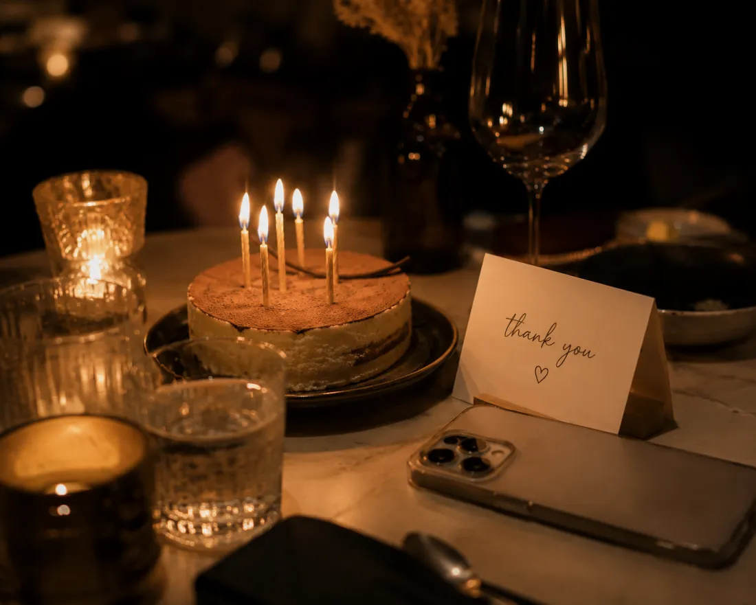 A candlelit birthday cake beside a handwritten note and a phone
